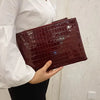 A woman holds a dark burgundy crocodile-embossed PU leather envelope clutch against a white background.