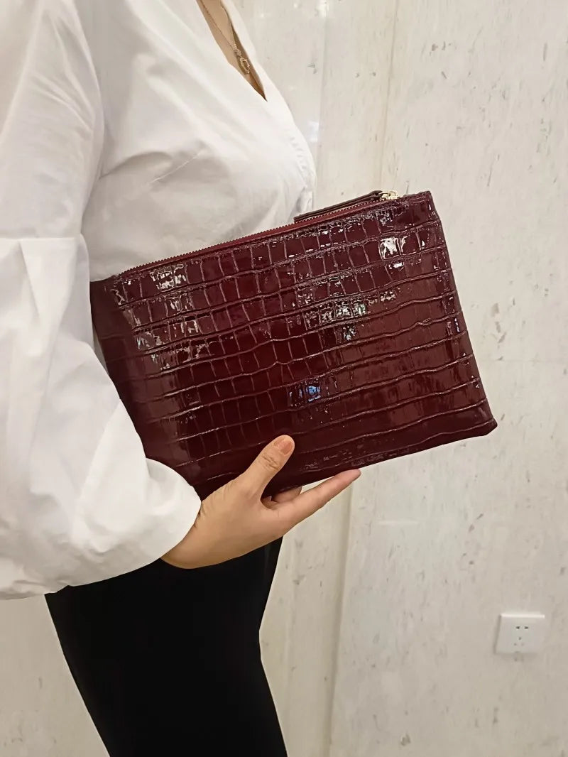 A woman holds a dark burgundy crocodile-embossed PU leather envelope clutch against a white background.