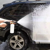 A hand is using a foam cannon with metal nozzles to wash the exterior of a black SUV.