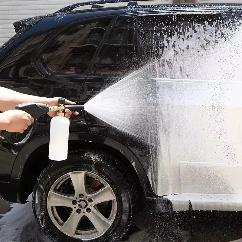 A hand is using a foam cannon with metal nozzles to wash the exterior of a black SUV.