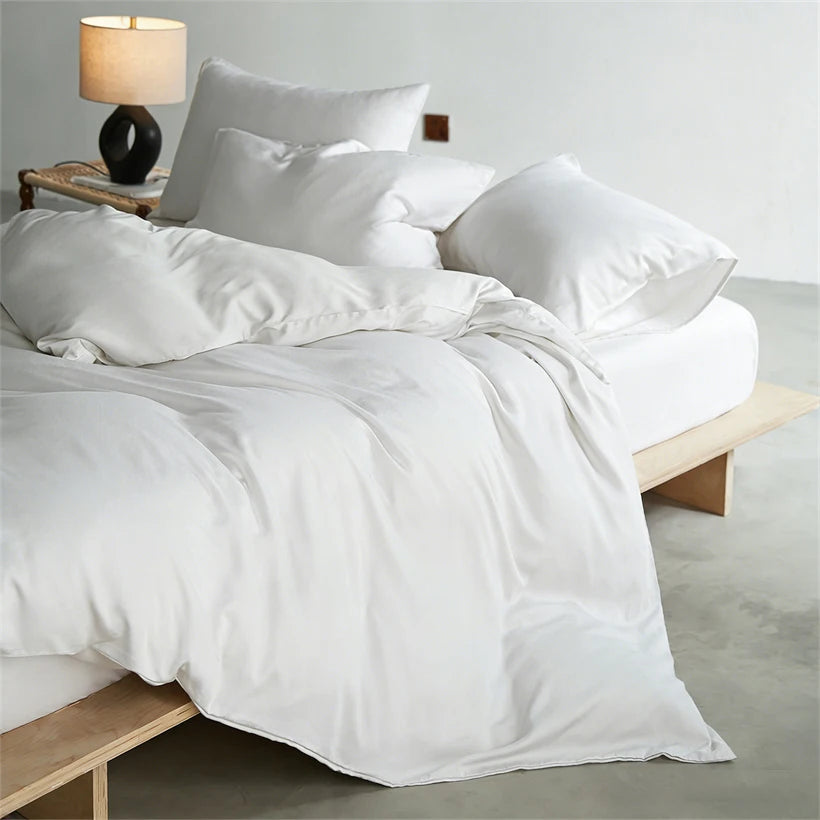White luxury mulberry silk duvet cover set displayed on a bed with white pillows and a lamp.