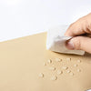 A hand is applying a self-adhesive white repair patch onto a beige PU leather surface.