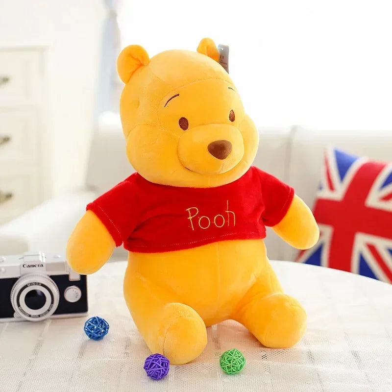 A yellow Winnie the Pooh plush toy bear sitting on a white surface with a camera and colorful balls.
