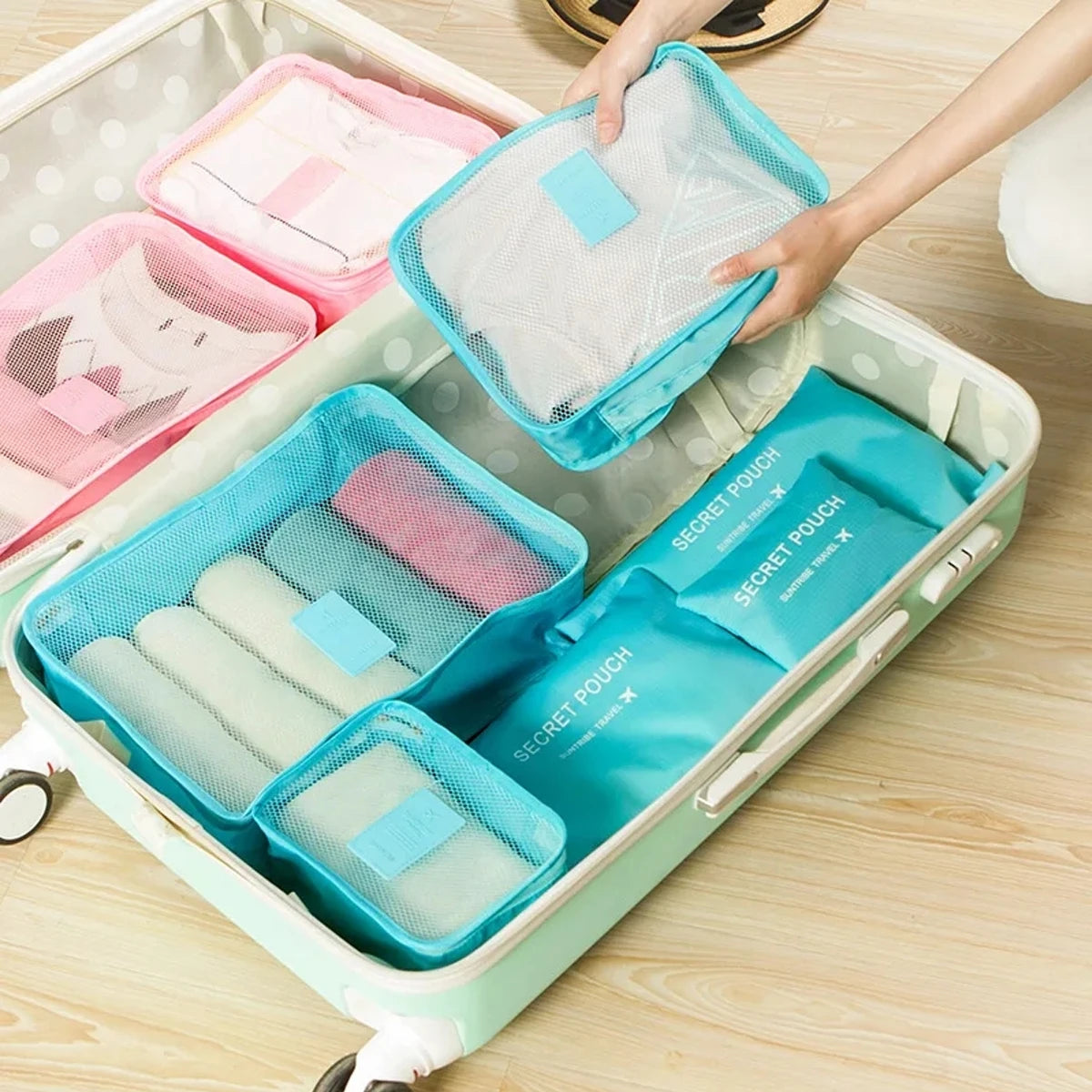 A light green packing cube set with six individual cubes and a mesh pouch is shown inside a storage box.