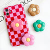 A pink and red checkered phone case with three flower-shaped grips in shades of pink, yellow, and brown.