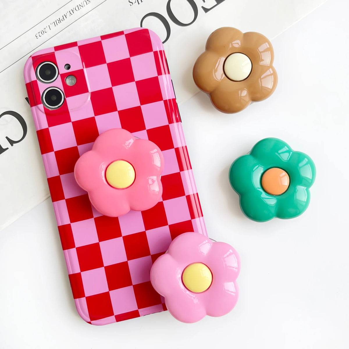 A pink and red checkered phone case with three flower-shaped grips in shades of pink, yellow, and brown.
