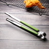 A pair of stainless steel BBQ tongs with green handles resting on a dark wooden surface next to a piece of fried food on a wi