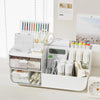 A white desk organizer with transparent drawers holding pens, pencils, and office supplies.