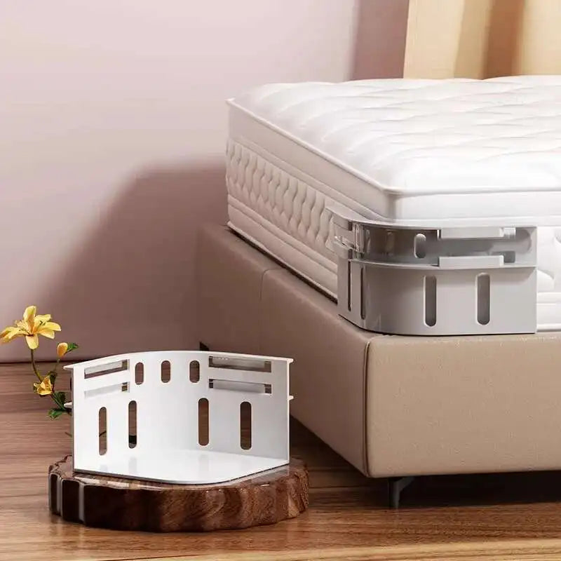 A white no-slip bed sheet holder clip is displayed on a wooden surface next to a white mattress.