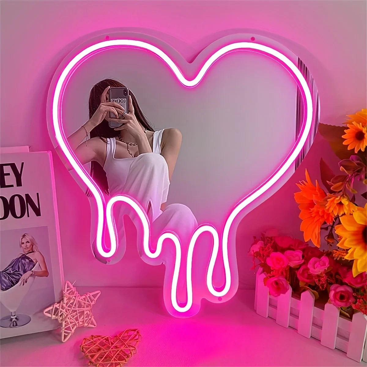 A neon sign shaped like a melting heart illuminates a pink room, featuring a woman posing in front of it.