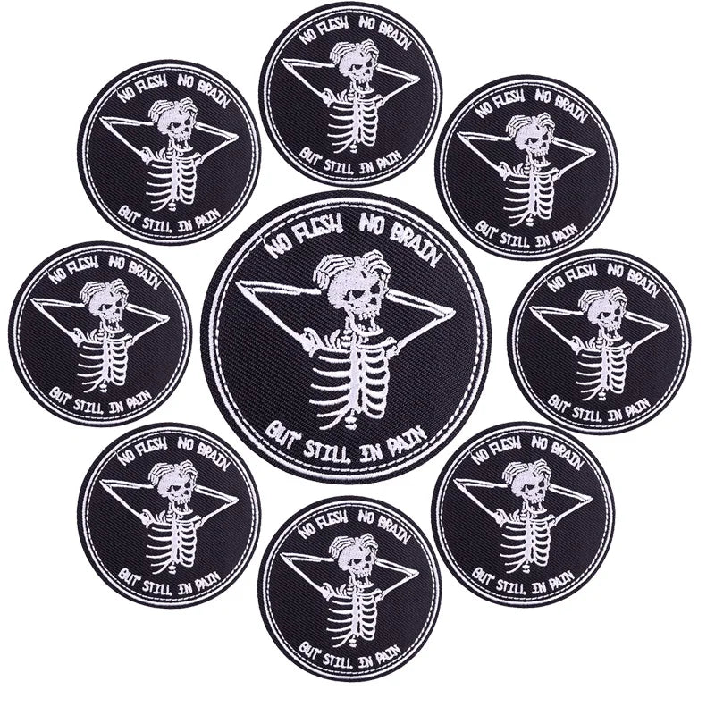Ten black embroidered iron-on patches featuring a skull and bones design with the text But Still In Pain