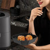 A woman is preparing food in a black reusable square air fryer with silicone liners on a stovetop.