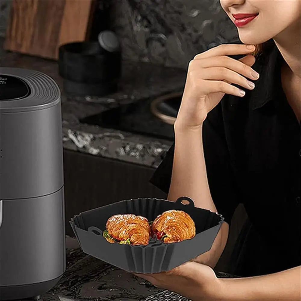 A woman is preparing food in a black reusable square air fryer with silicone liners on a stovetop.