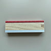 A wooden fingerboard ramp set featuring a quarter pipe and rail with a red top and light wood body.