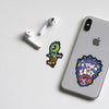 A white Apple AirPod case and a green skull sticker are displayed on a white surface.