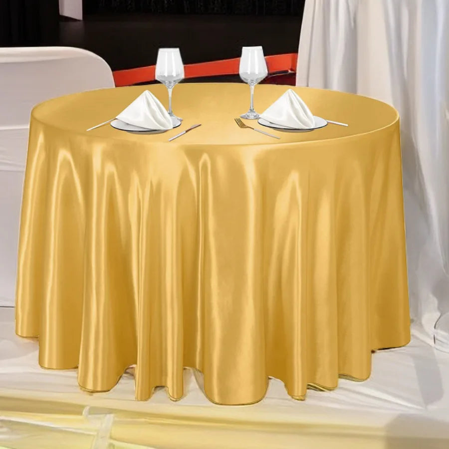 A round gold satin tablecloth set for an event or wedding, featuring white napkins and wine glasses.