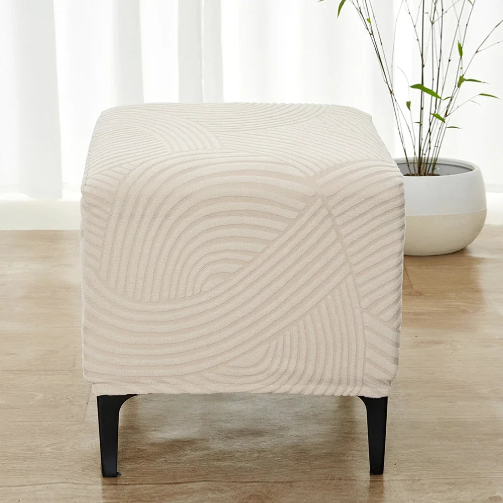 A beige geometric jacquard stretch ottoman cover placed on a wooden floor.