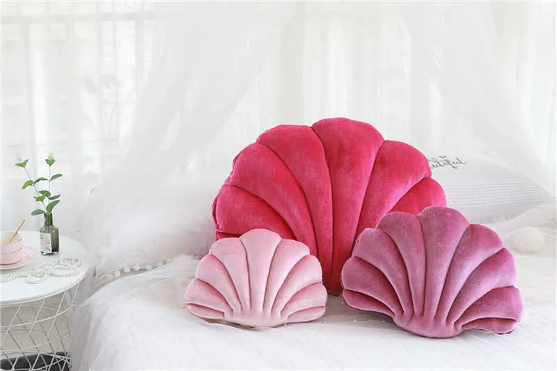 A collection of pink and magenta velvet shell print throw pillows resting on white bedding.