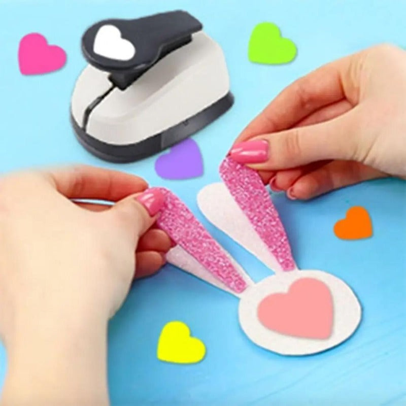 Hands are using a heart-shaped paper punch set for crafting on a light blue background.