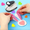 Hands are assembling a heart-shaped paper punch set for crafting on a light blue surface.