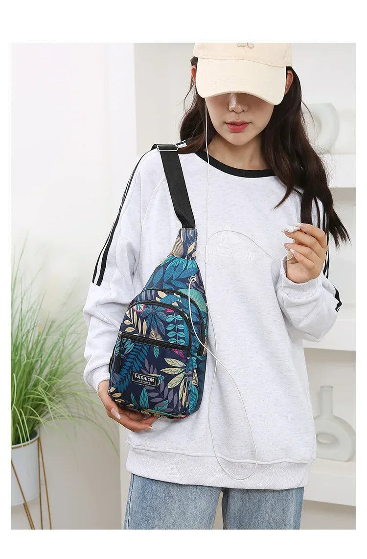 A woman wearing a light gray sweatshirt holds a colorful leaf print sling crossbody bag.