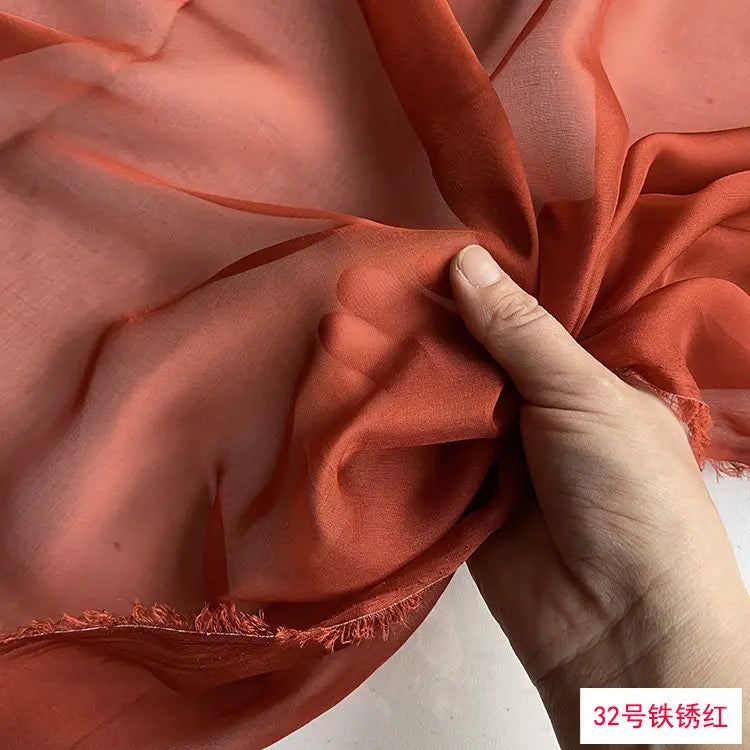 Close-up of flowing burnt orange silk chiffon fabric being gathered by a hand