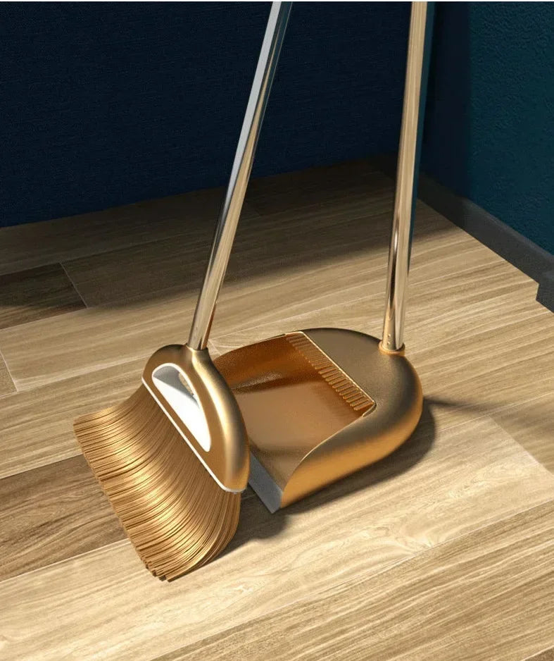 A golden broom and dustpan set with a floor wiper resting on a wooden floor.