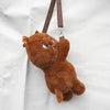 A brown, fluffy teddy bear plush doll hanging by a brown strap against a white background.