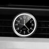 A close-up of a round quartz clock with luminous hands mounted on a black car vent grille.