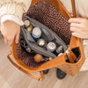 A close-up of a brown leather purse showing an organizer insert with multiple compartments and various small bottles.