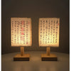 A pair of Chinese style table lamps with linen shades and wooden bases, illuminated against a dark background.