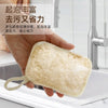 A hand holds a natural loofah body scrubber with a hanging rope, positioned above a kitchen sink.