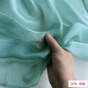 A hand is gently folding a piece of light mint green sheer silk chiffon fabric.