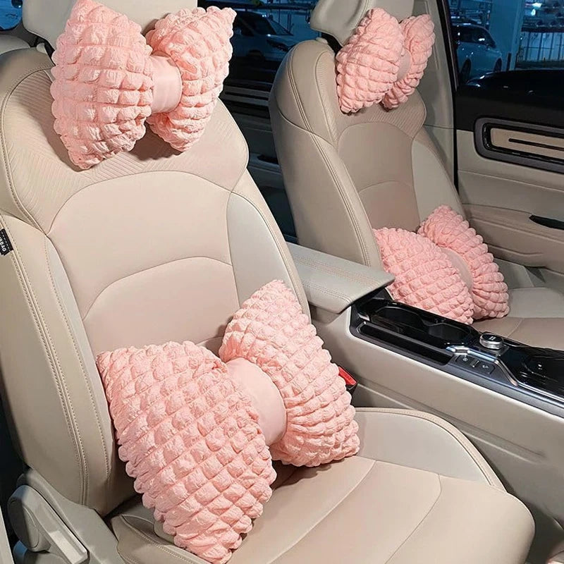 Pink bowknot car neck pillows with lumbar support placed on a light-colored car seat interior.