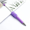 A purple ballpoint pen with a sparkly purple sequin tip resting on a white background next to green foliage.