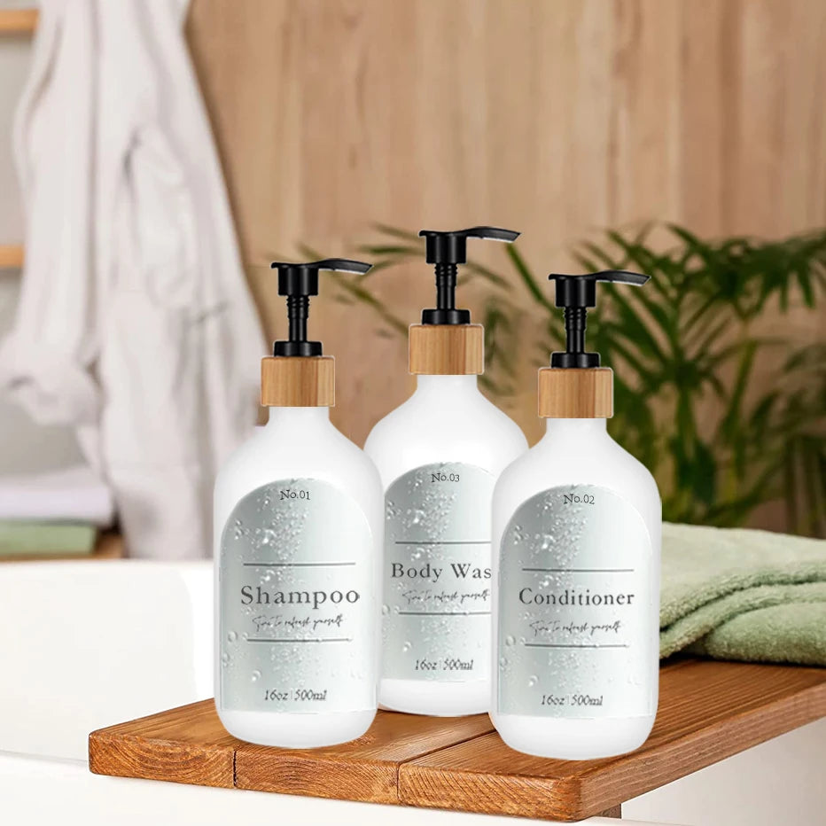 Three white refillable soap dispenser bottles for shampoo conditioner and body wash sitting on a wooden tray
