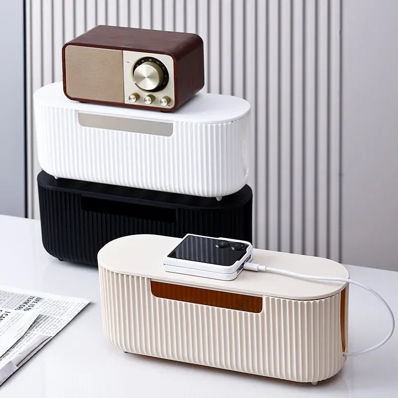 A white cable management box with a brown top organizer and a black power strip visible on a desk.