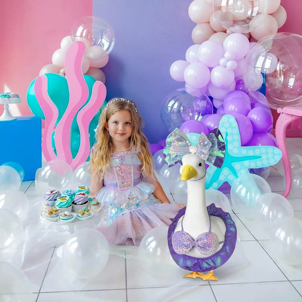 A mermaid bikini costume is displayed next to a lawn goose statue surrounded by balloons and sweets.