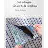 A hand is applying a clear self-adhesive tear and paste to refresh a dark, reflective panel on a wooden surface.