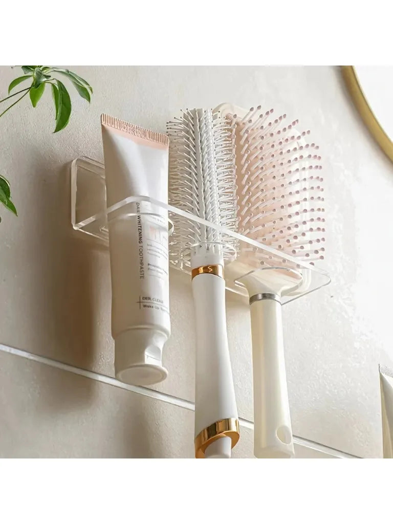 Wall-mounted acrylic organizer holding a white hairbrush and a pink round brush.