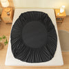 A black soft brushed fitted sheet with an elastic edge is displayed on a white bed frame.