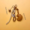 A braided leather croissant keychain with a bag pendant displayed on a beige background.