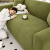 A person is relaxing on a moss green stretch jacquard sofa cover while drinking tea.
