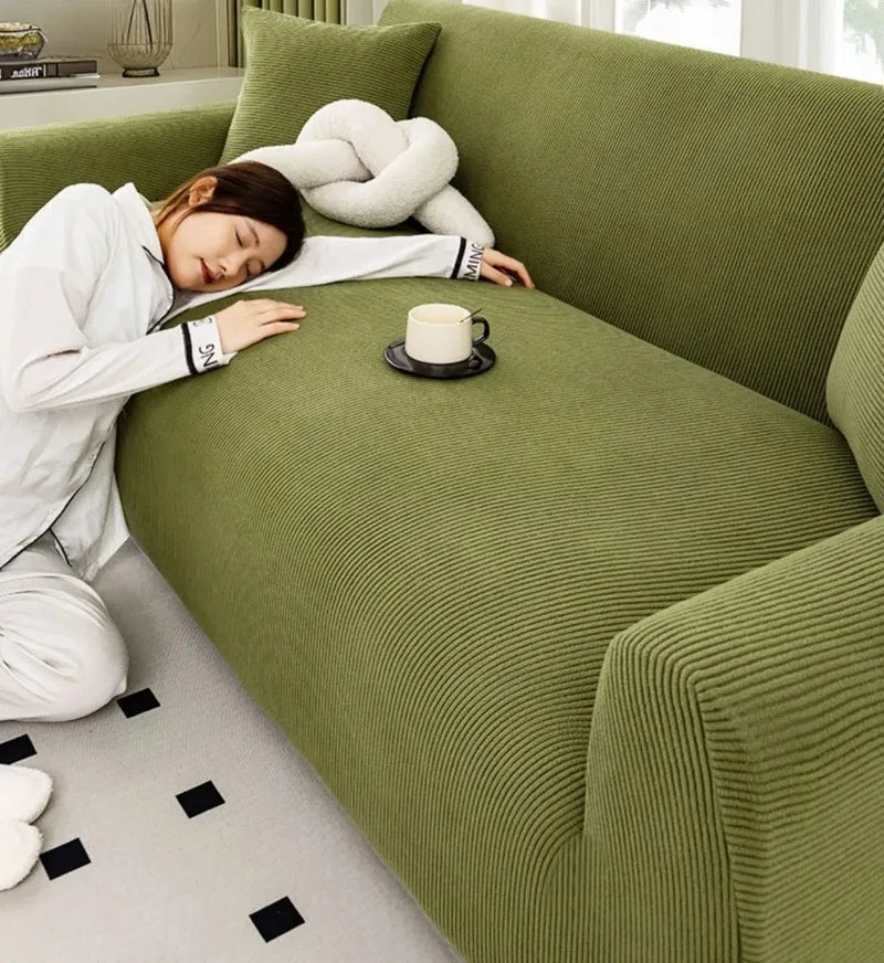 A person is relaxing on a moss green stretch jacquard sofa cover while drinking tea.