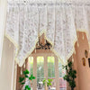 White lace curtain valance with gold trim and dangling beads decorating a window frame.