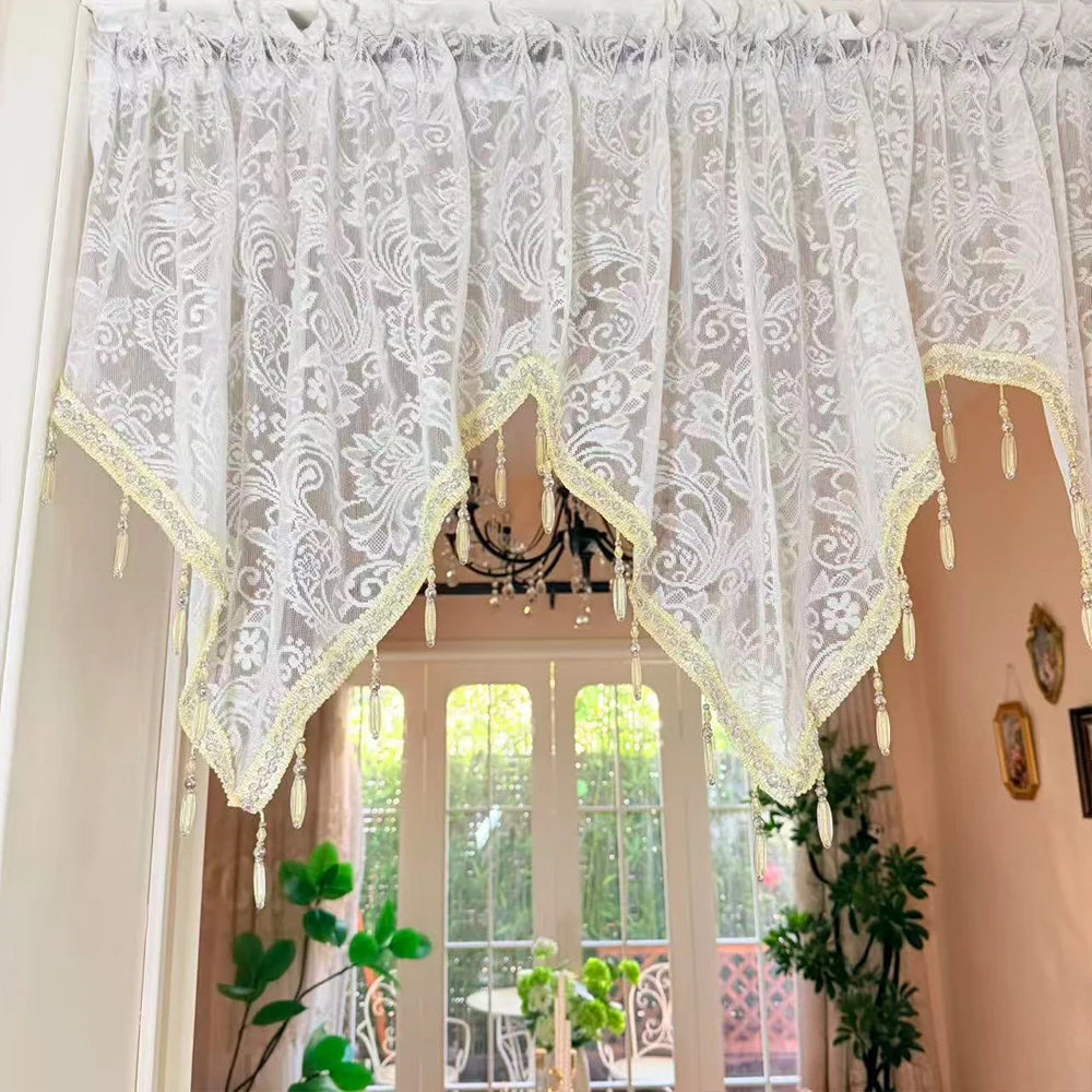 White lace curtain valance with gold trim and dangling beads decorating a window frame.
