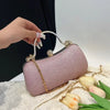 A hand holds a light purple shimmering envelope clutch with a gold chain strap resting on white fabric.