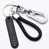 Silver keychain featuring a personalized phone number engraved on a black tag and attached to a braided leather rope.