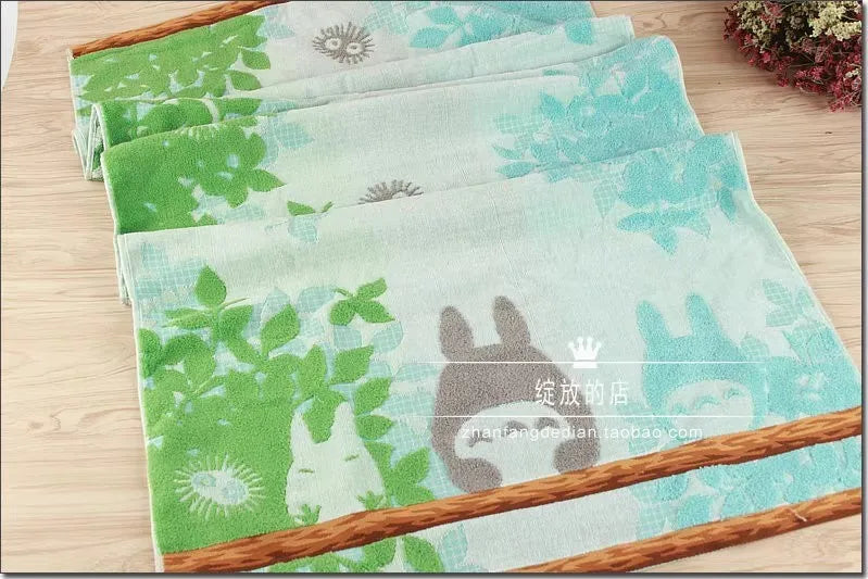A stack of light green and teal embroidered cartoon face towels with natural wood trim.