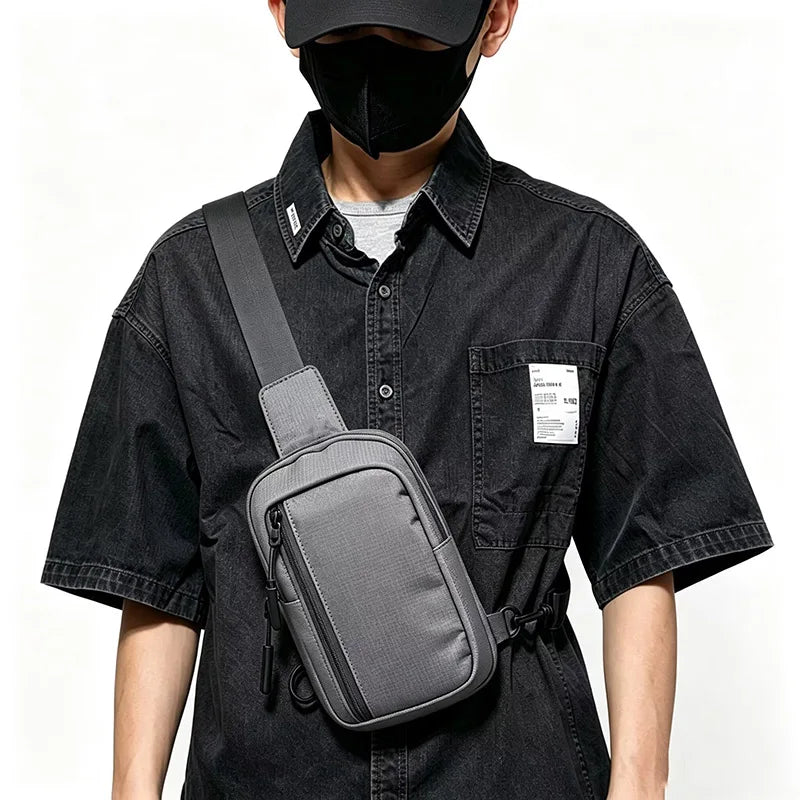Eine Person in einem schwarzen Shirt und Gesichtsmaske hält eine graue Umhängetasche.